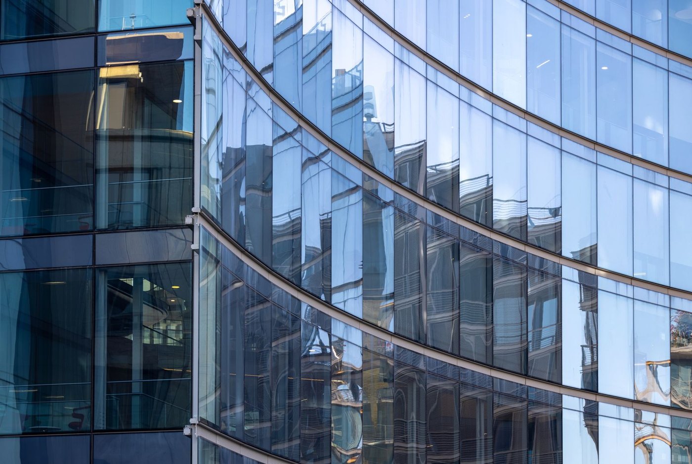 Curved facade glass reflecting the street: the geometry premium buys what flat panels cannot.